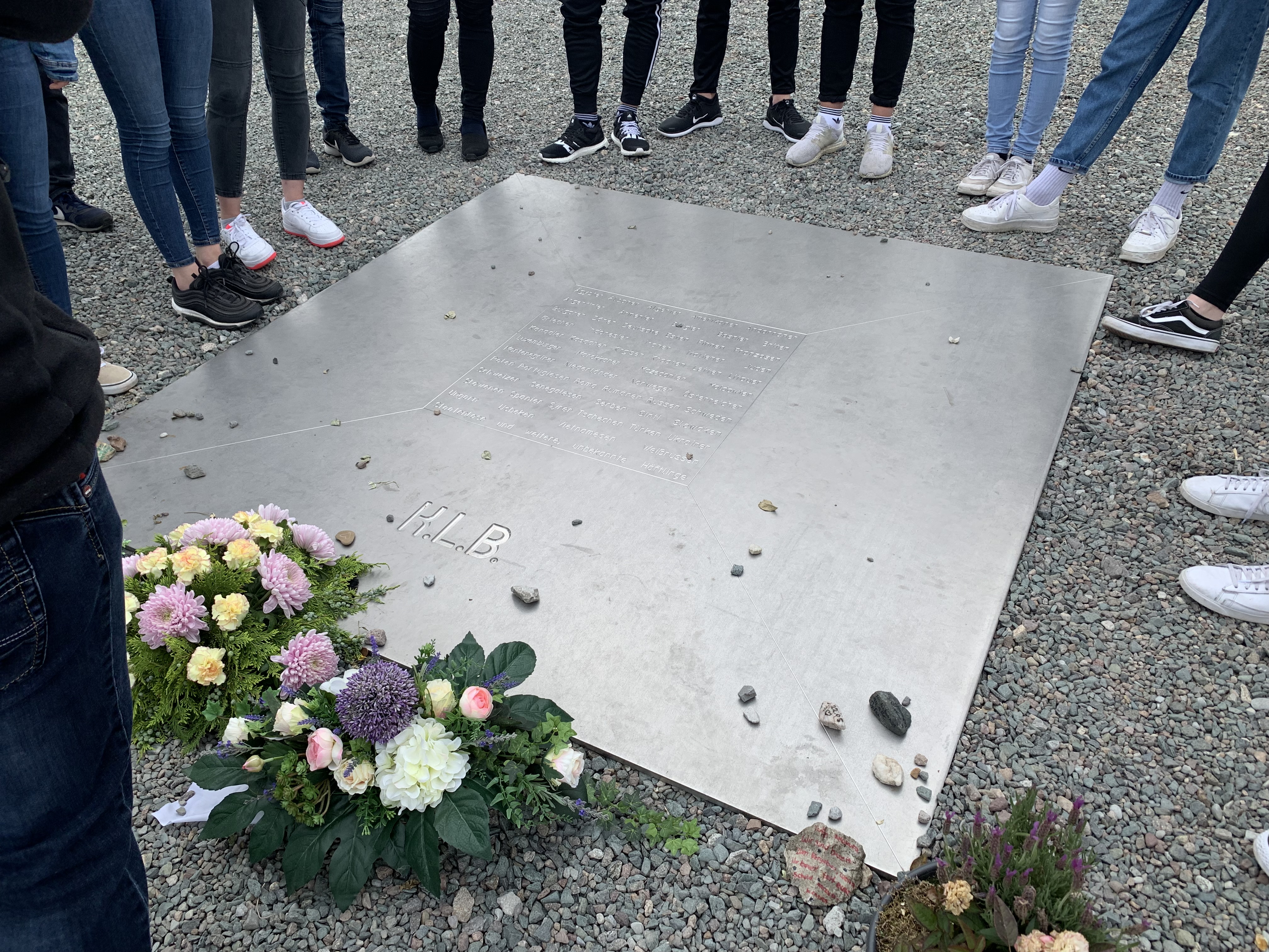 Das Bild zeigt die Füße von Teilnehmer*innen am Projekt Hinsehen-Nachdenken-Handeln, die das zentrale Denkmal auf dem Appellplatz des Konzentrationslagers rahmen.